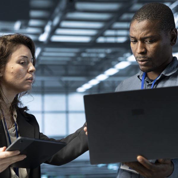 System administrators using laptop in data center, managing server virtualization. IT specialists using notebook in server room, sustaining long term infrastructure reliability